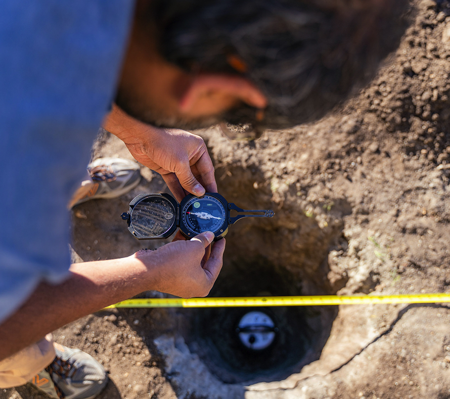A scientist takes a compass heading over an instrument being buried in the ground