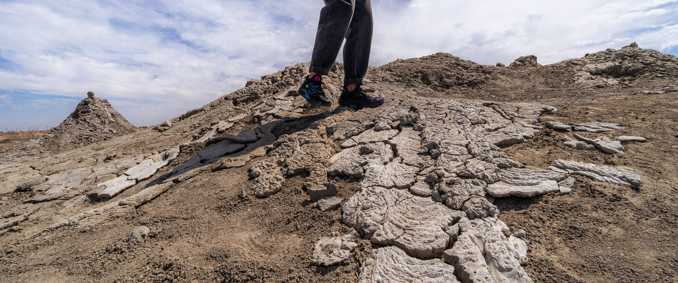 A woman walking over the dried, cracked surface of a mud volcano
