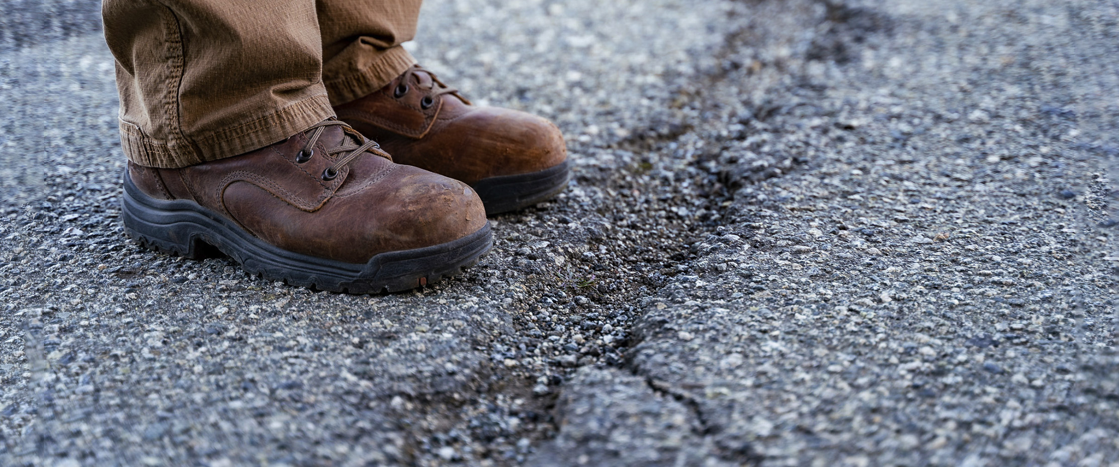 A pair of scientist’s boots standing on the edge of a jagged crack in a road